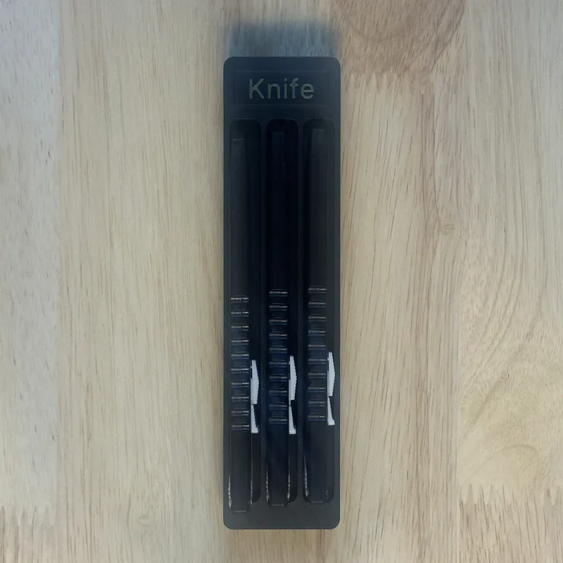A narrow shadowbox labeled Knife, holding three knives
